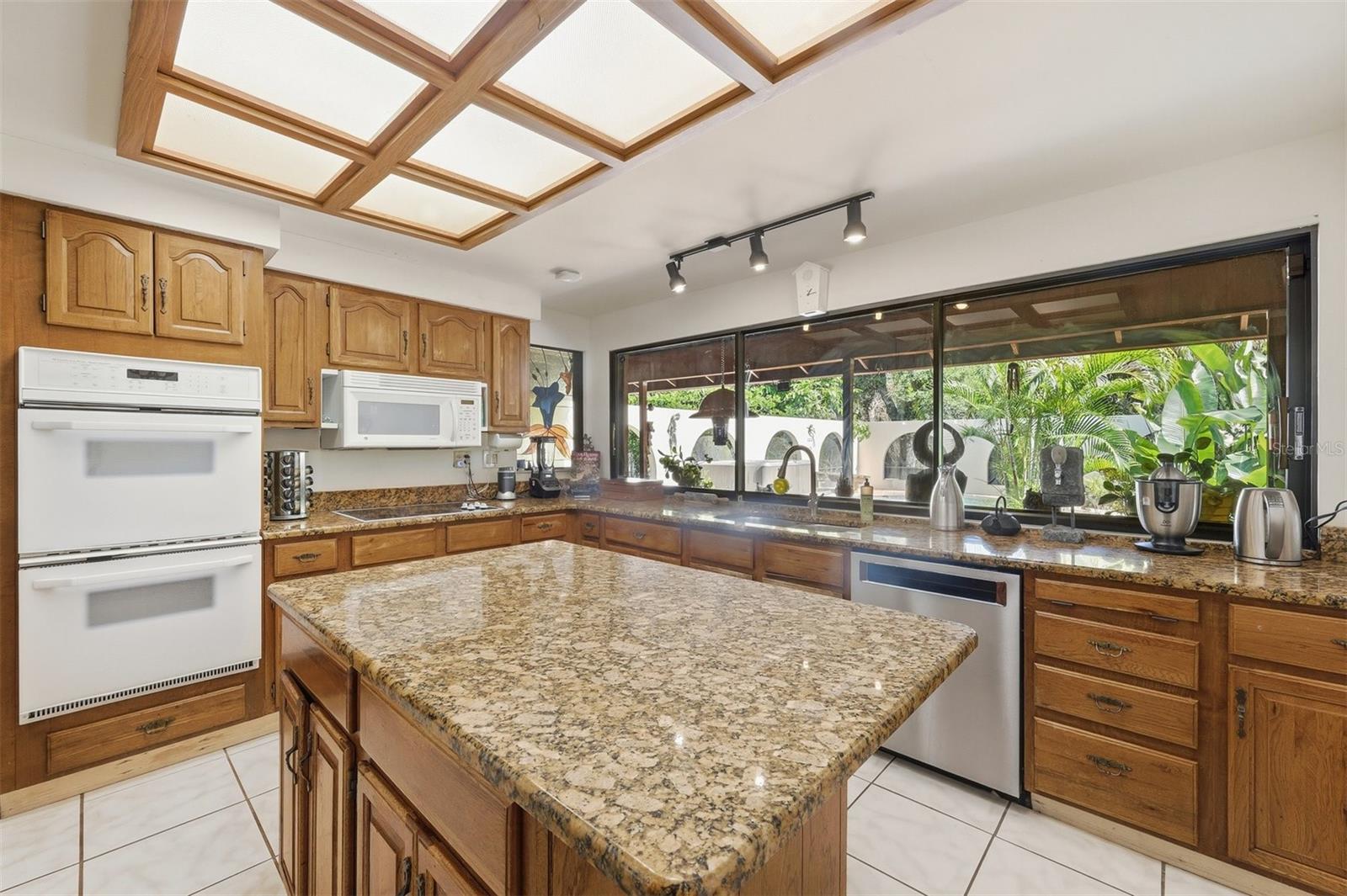 Kitchen with Double Ovens, Granite Counters and Wall of Windows Overlooking Pool & Gardens