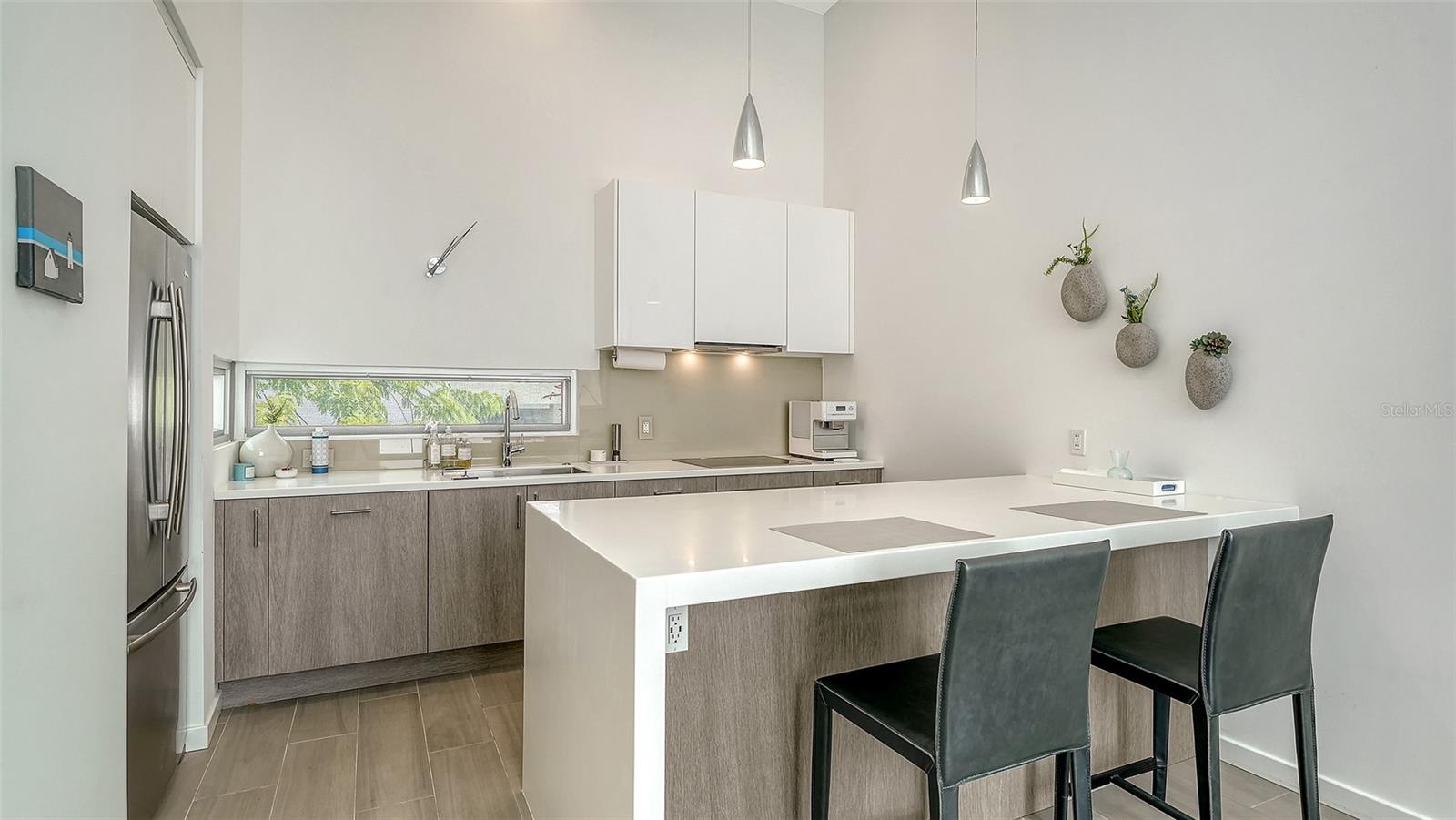 Contemporary kitchen with solid surface countertops and waterfall-edge island and SS appliances, including Miele induction range & Miele d/w, hood, and oven/microwave