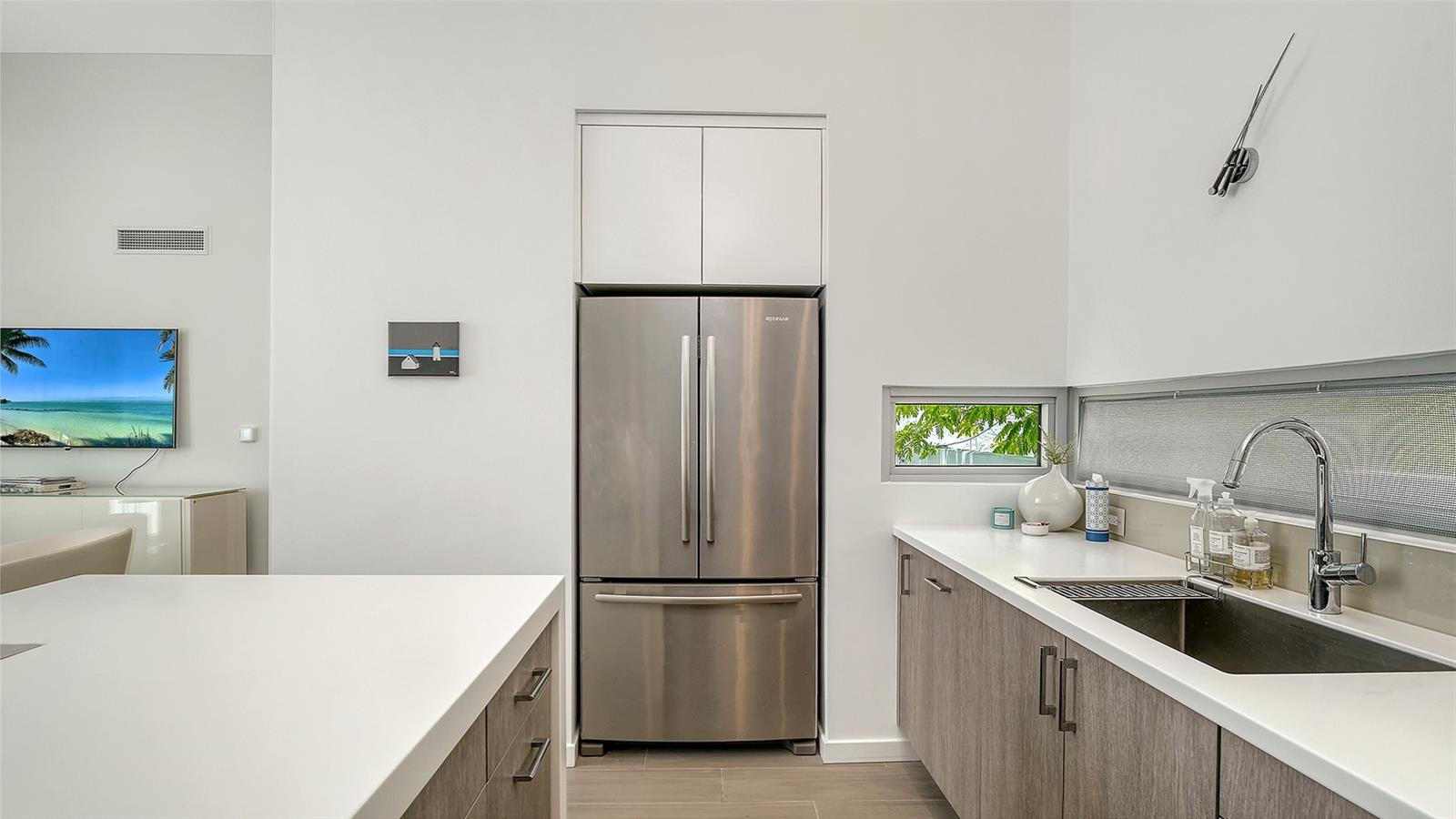 Contemporary kitchen with solid surface countertops and waterfall-edge island and SS appliances, including Miele induction range & Miele d/w, hood, and oven/microwave.
