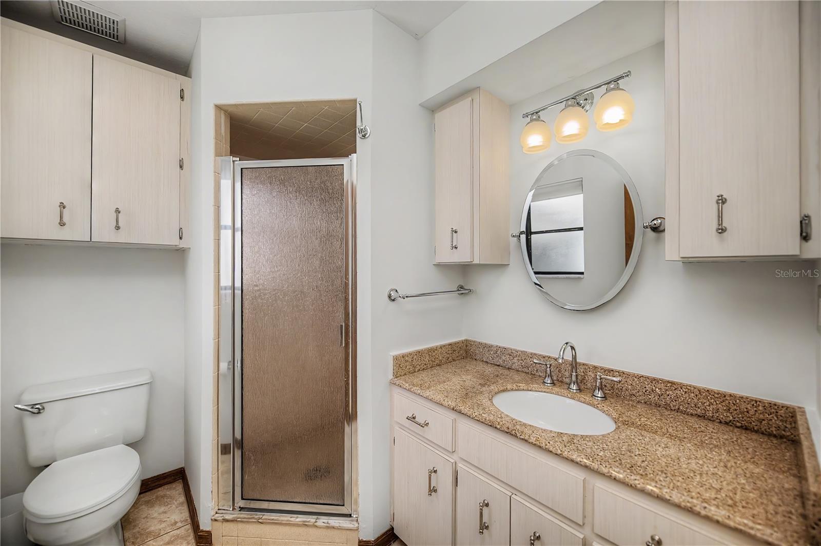 Primary Bathroom with Granite Vanity, Built In Storage, and Glass Enclosed Shower.