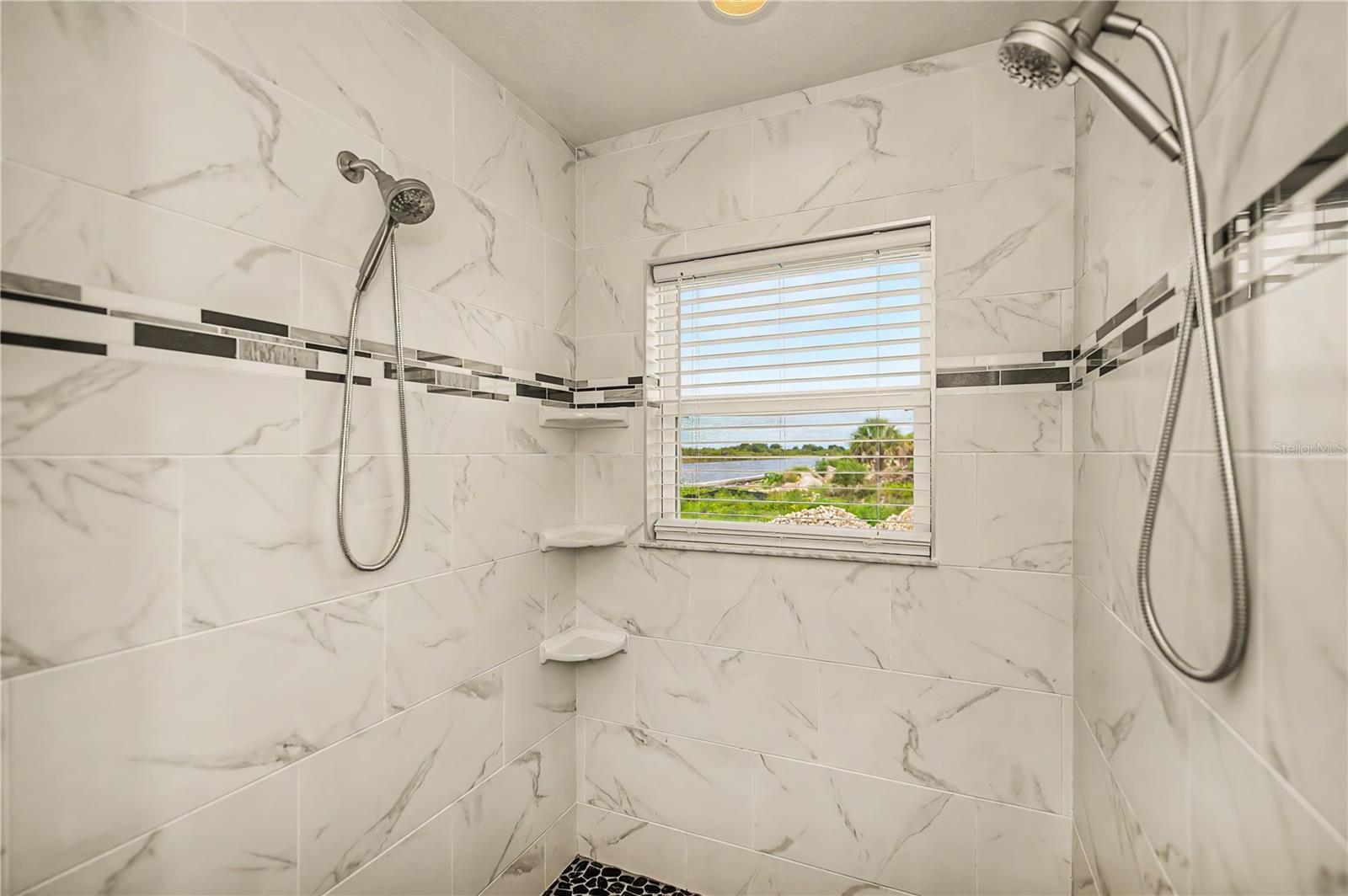 Spa-Like Roman Shower with Dual Showerheads and a Window Framing Serene Water Views.