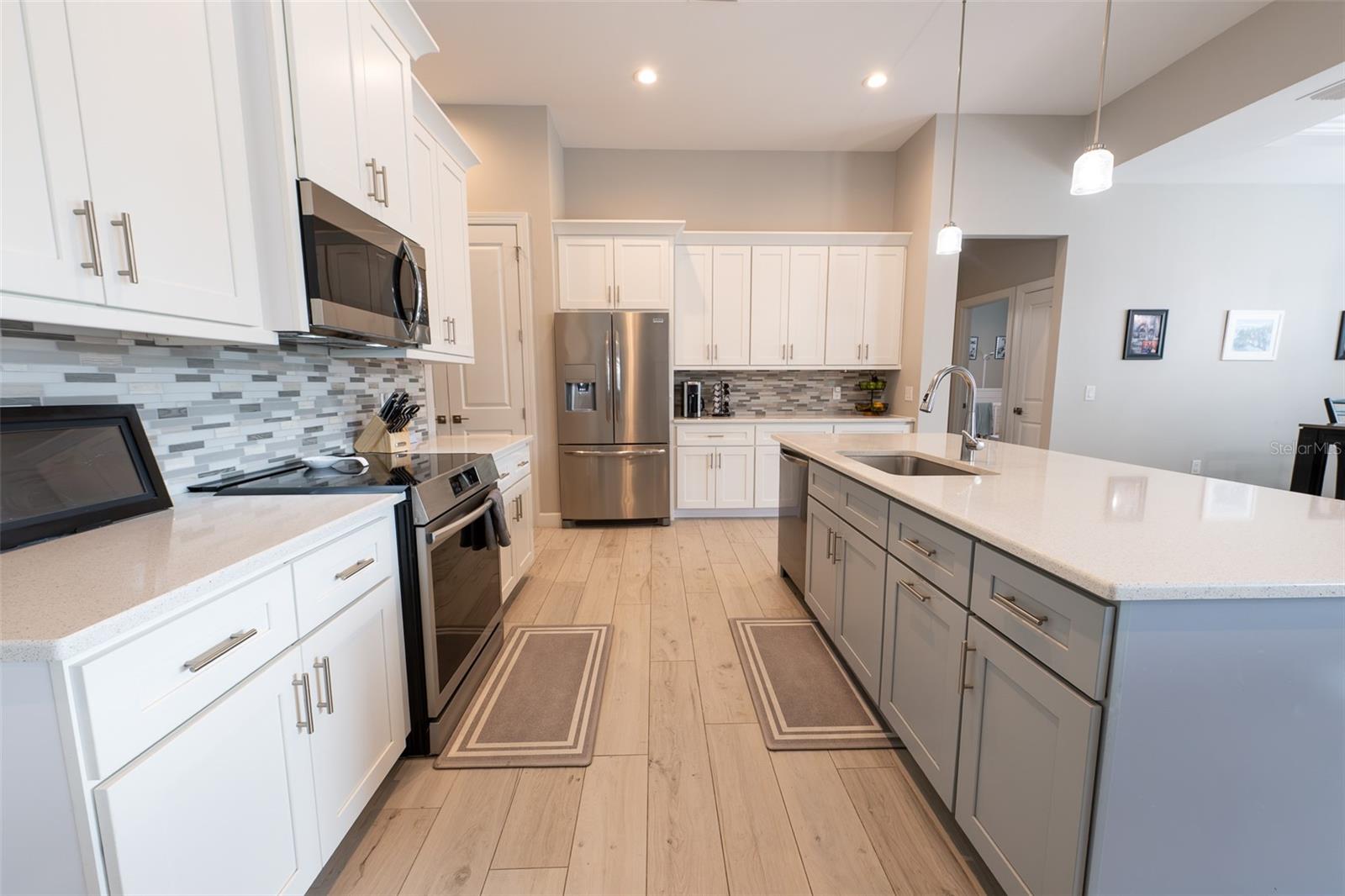 Pristine perspective of the kitchen showing the premium stainless steel range, undermount sink, and the contrast between the clean white perimeter cabinetry and the contrasting soft gray/blue island. Modern design meets everyday comfort in this Punta Gorda masterpiece.