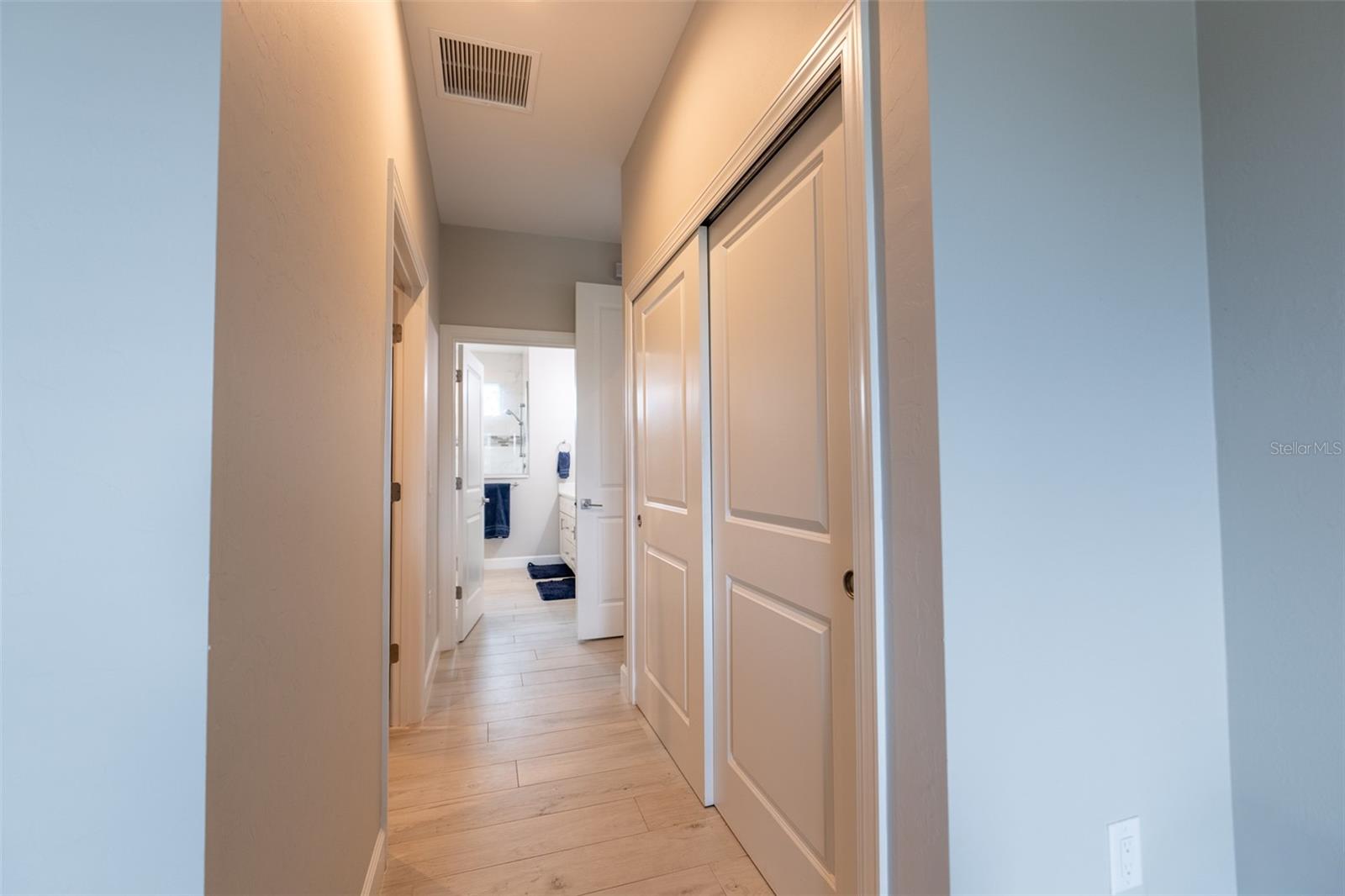 This wide hallway view highlights the desirable split floor plan layout, connecting the primary retreat to the main living spaces. Features include solid-core interior doors, uniform tile flooring, and large storage closets.
