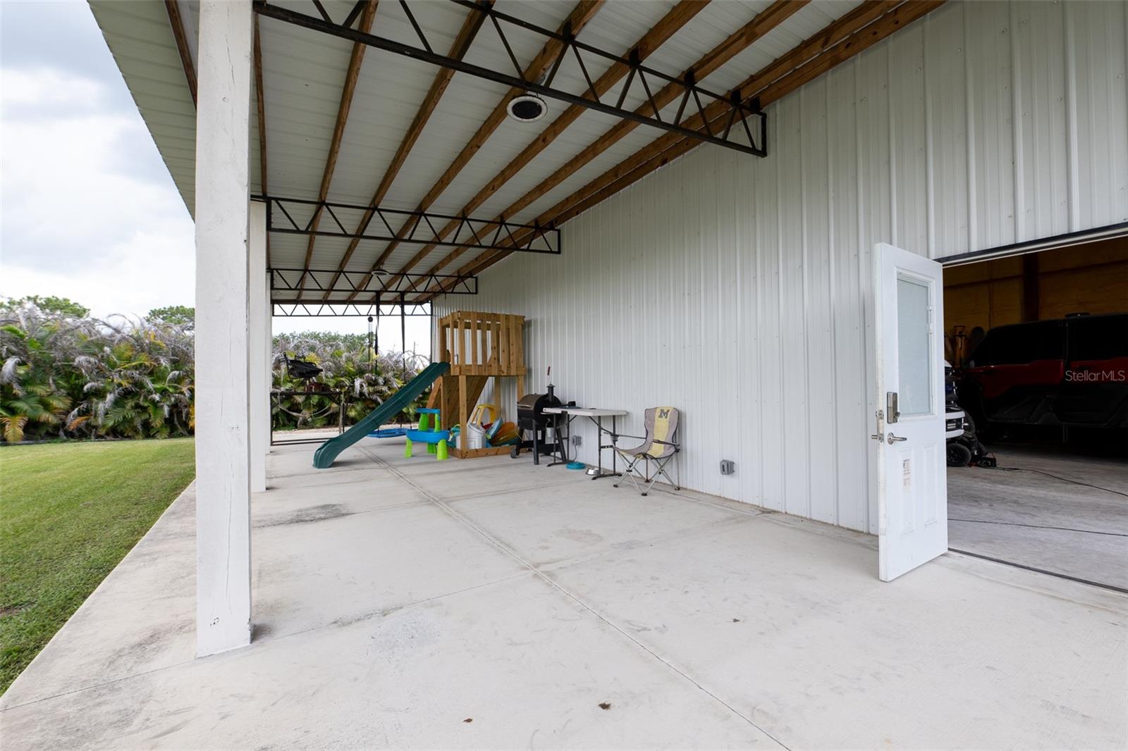 A closer look at the expansive concrete pad underneath the detached building’s massive covered overhang. This versatile space provides excellent shade and endless options for outdoor entertaining, working on projects, or additional vehicle parking.