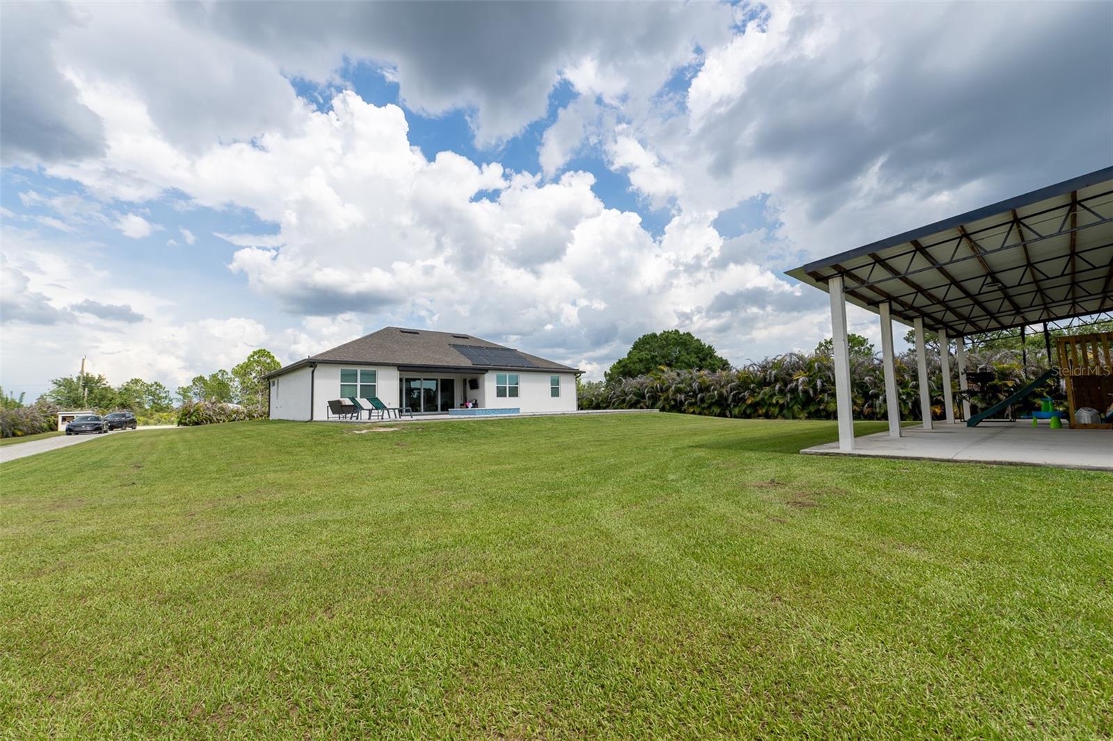 Sprawling wide-angle view of the massive backyard lawn separating the primary residence and the massive outbuilding. This premium acreage lot offers limitless potential for additional landscaping, gardening, or a secure compound setup.
