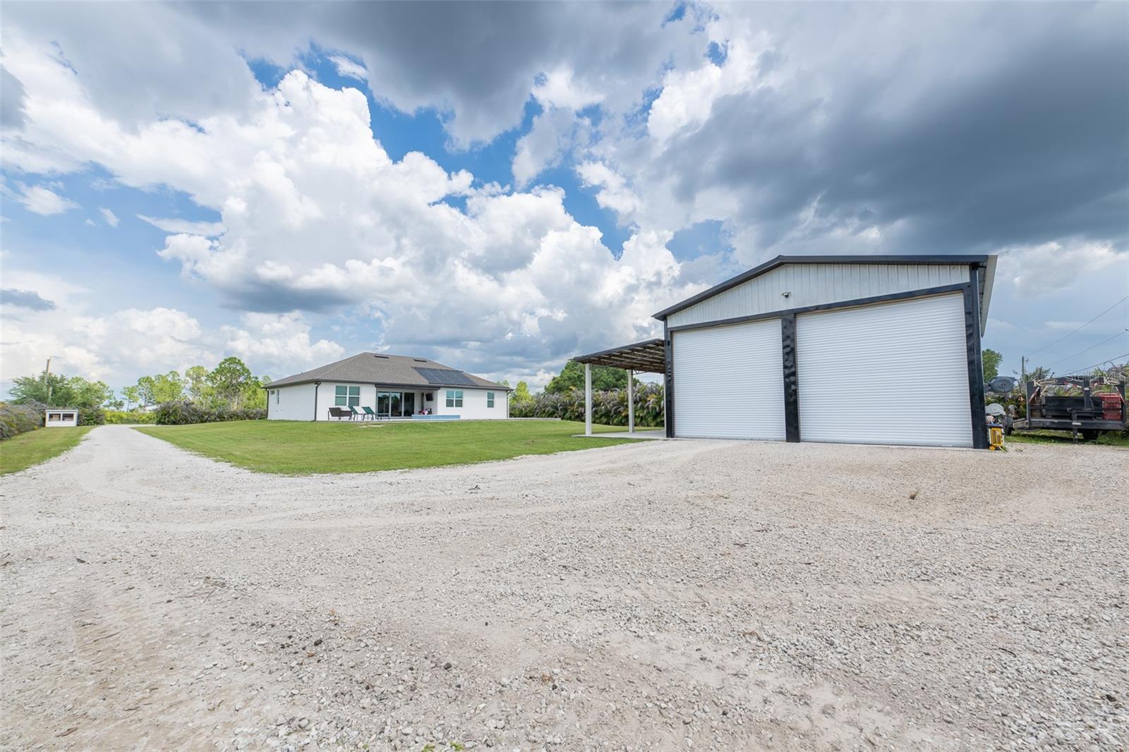 Comprehensive property overview showing the expansive gravel driveway, massive detached workshop garage, and the main pool residence in the distance. An exceptional find for buyers seeking land, premium storage, and a modern custom home with no HOA restrictions.