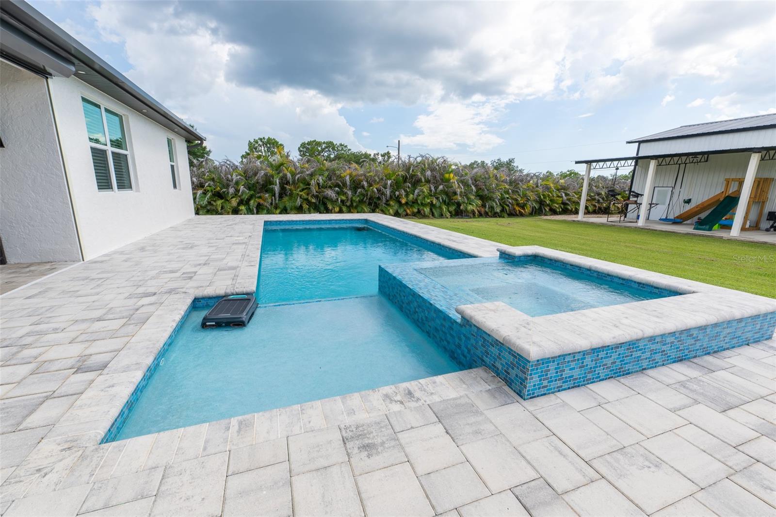 Dive into luxury! This close-up view of the spectacular custom swimming pool highlights the oversized sun shelf (baja shelf) perfect for lounging, a built-in raised spa with premium blue mosaic tile inlay, and a durable, expansive paver deck designed for low-maintenance outdoor living.