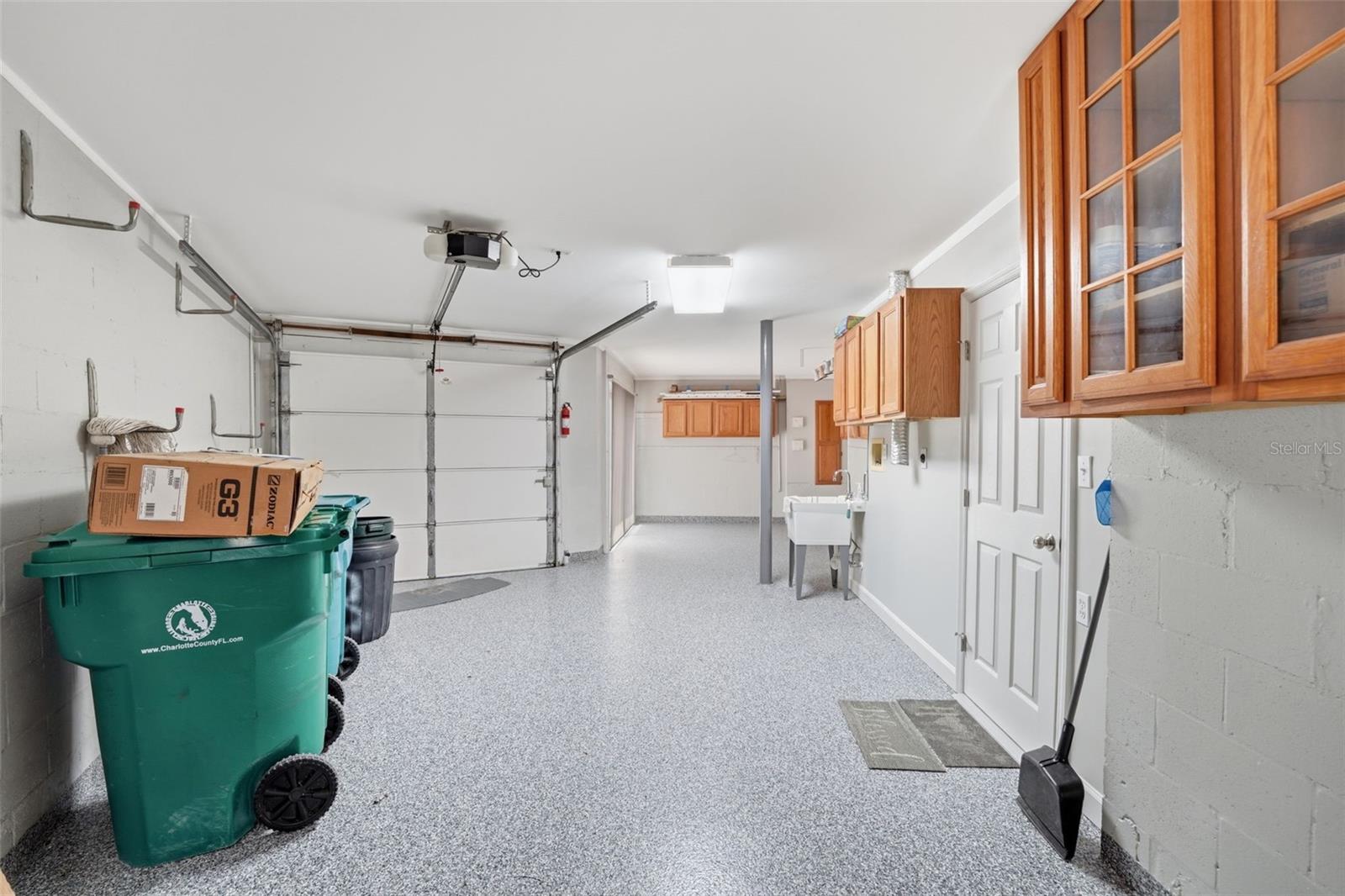 GARAGE SHOWING LAUNDRY TUB, WALL CABINETS & DOORWAY TOWARD POOL LOUNGE AREA
