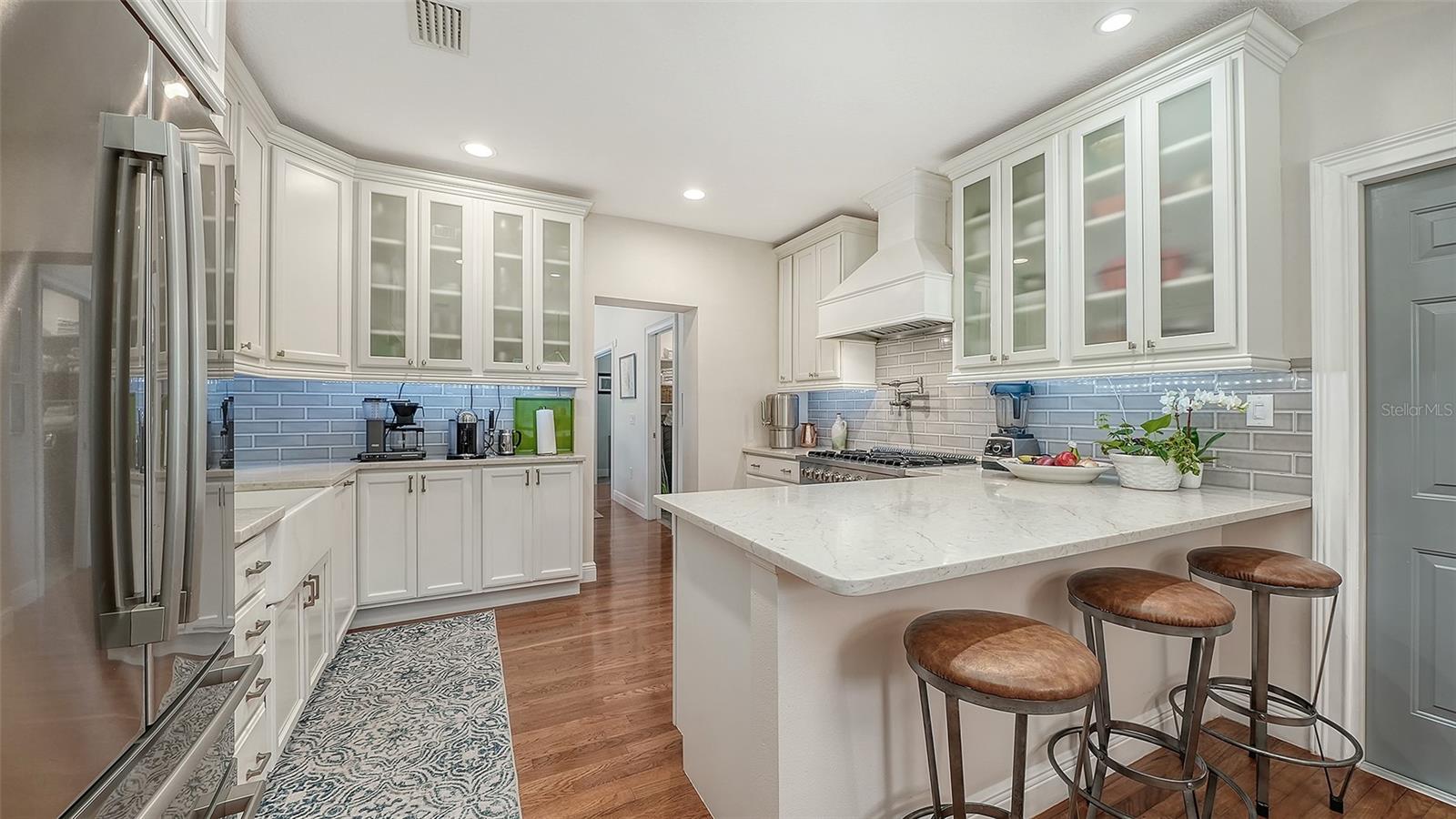 Bright gourmet kitchen showcases custom cabinetry, glass-front storage, quartz surfaces, and an oversized island with seating.