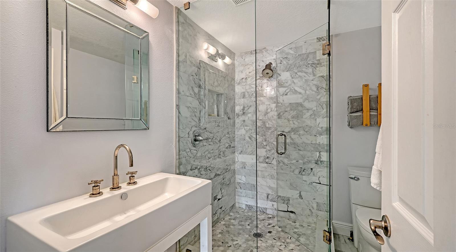 Renovated en-suite bathroom features a sophisticated walk-in glass shower, elegant vanity, and upscale finishes.
