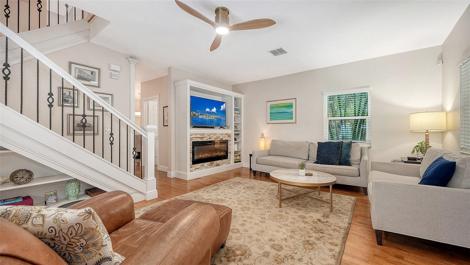 Bright, sophisticated living room features rich hardwood floors, an electric fireplace, custom built-ins, and refined coastal-inspired furnishings.